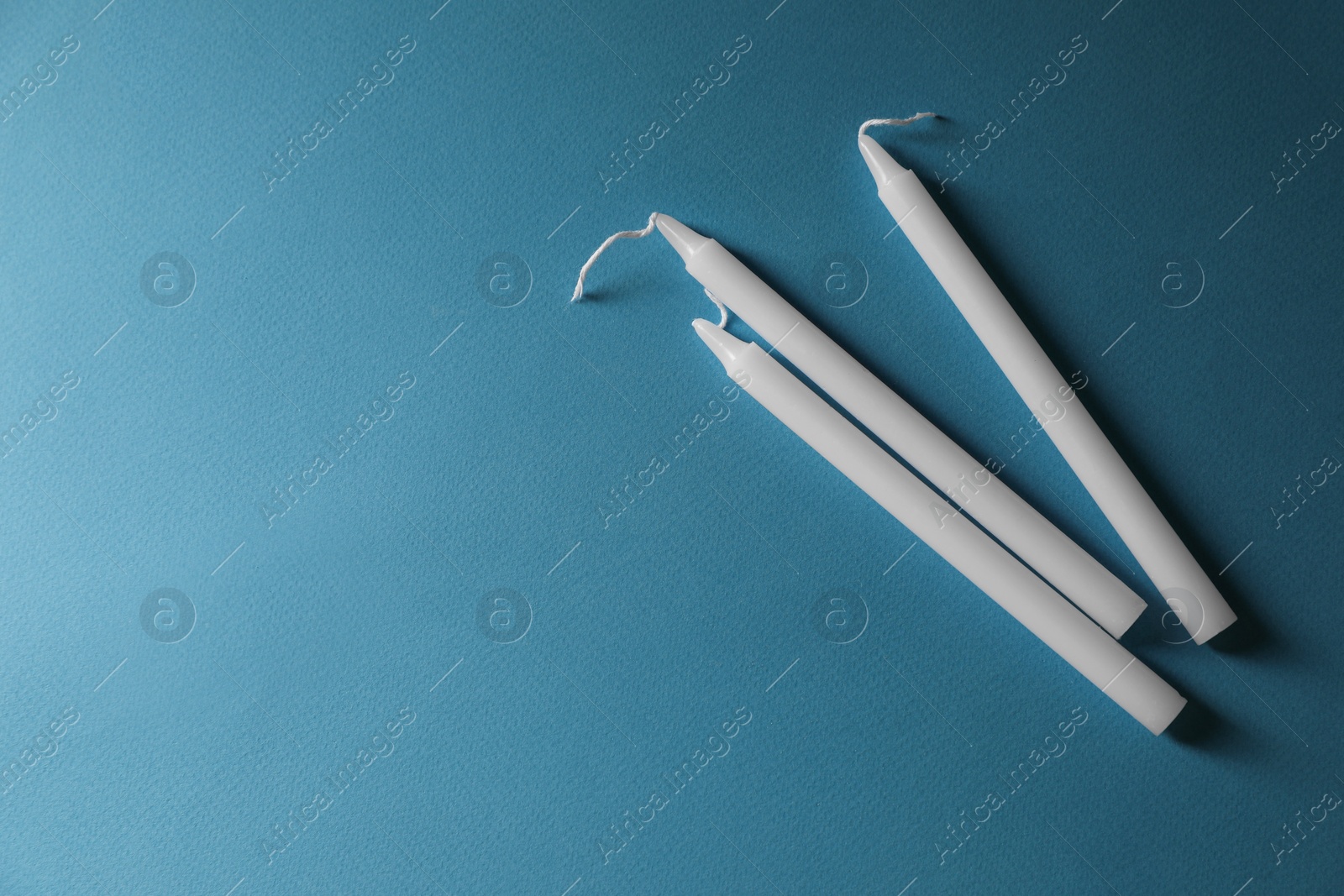 Photo of Church wax candles on light blue background, flat lay and space for text