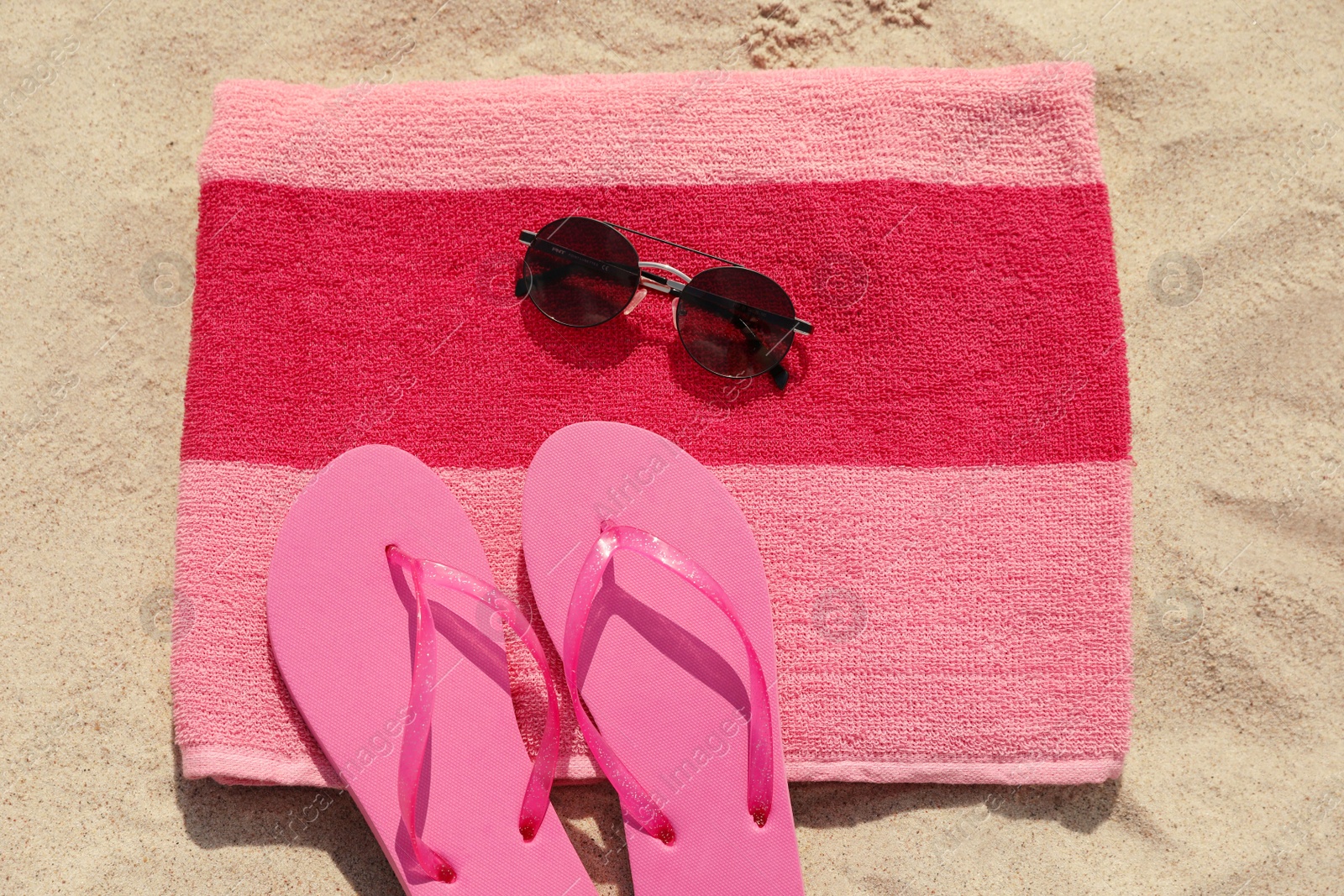 Photo of Beach towel with slippers and sunglasses on sand, flat lay