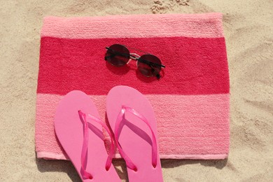 Beach towel with slippers and sunglasses on sand, flat lay