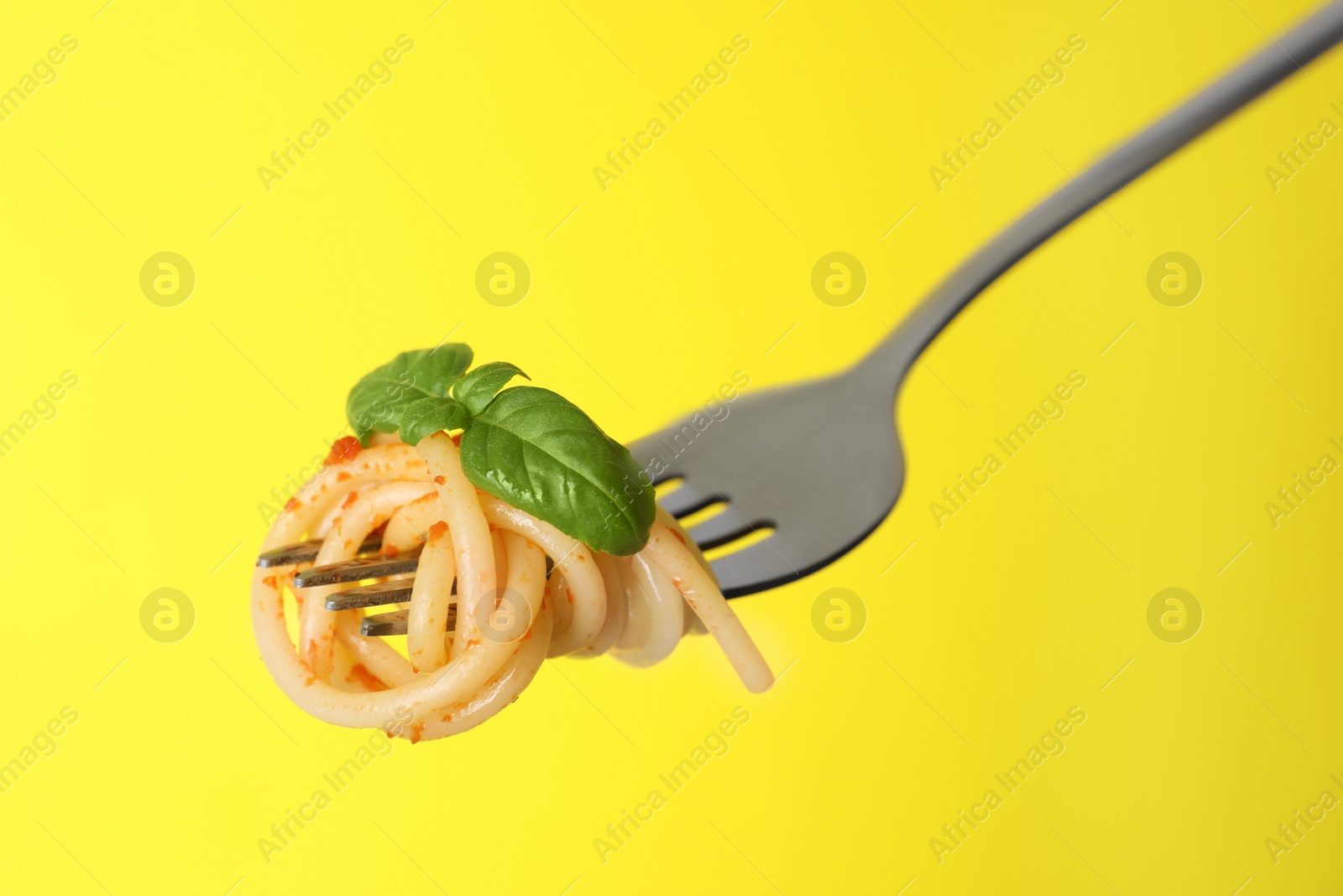 Photo of Fork with tasty pasta, basil and tomato sauce on yellow background, closeup