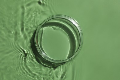 Photo of Stylish presentation for product. Glass podium in water on pale green background, top view