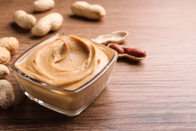 Photo of Yummy peanut butter in glass bowl on wooden table, space for text