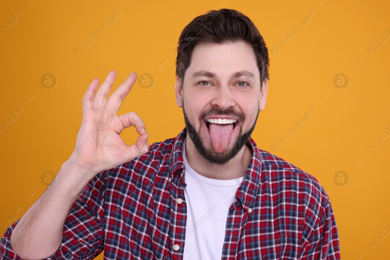 Photo of Happy man showing his tongue and making ok gesture on orange background