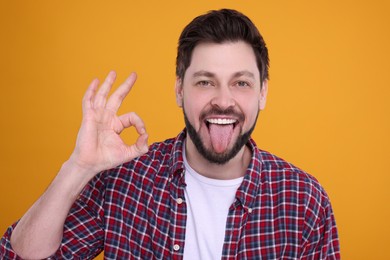 Happy man showing his tongue and making ok gesture on orange background