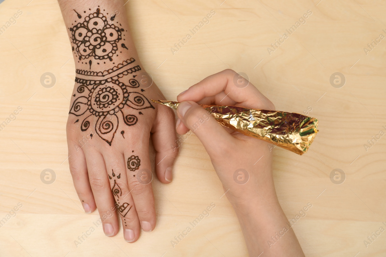 Photo of Master making henna tattoo on hand, top view. Traditional mehndi