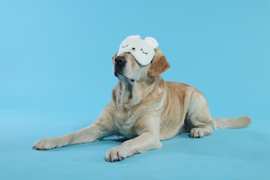 Photo of Cute Labrador Retriever with sleep mask resting on light blue background