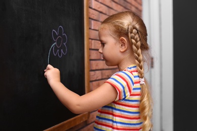 Cute little left-handed girl drawing on chalkboard near brick wall