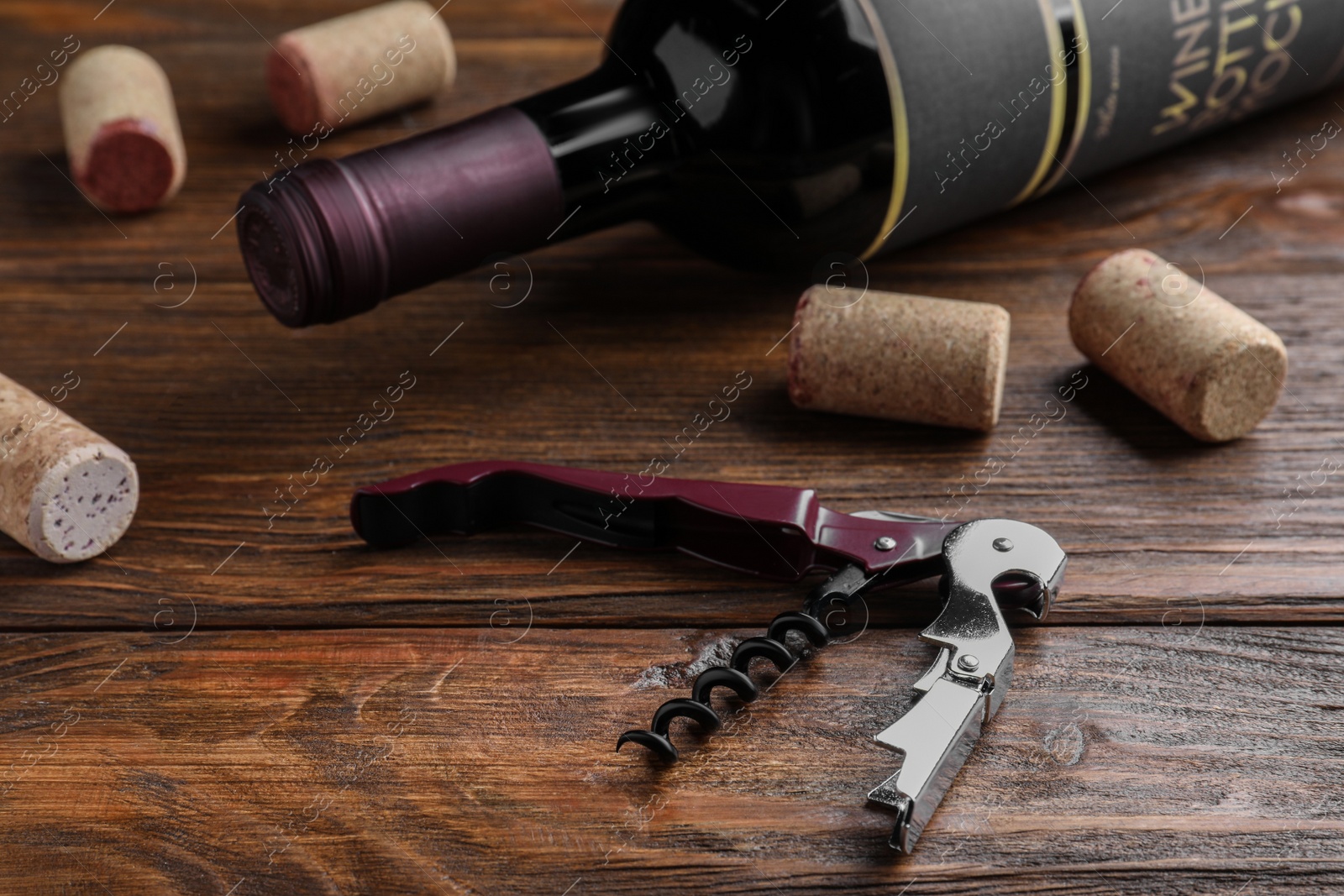 Photo of Corkscrew, wine bottle and stoppers on wooden table.