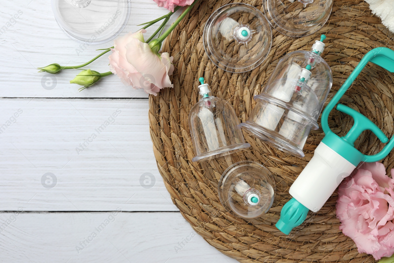 Photo of Plastic cups, hand pump and flowers on white wooden table, flat lay with space for text. Cupping therapy