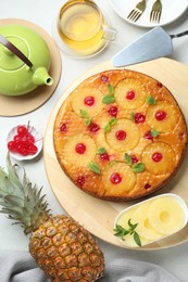 Tasty pineapple cake served with tea and ingredients on white table, flat lay