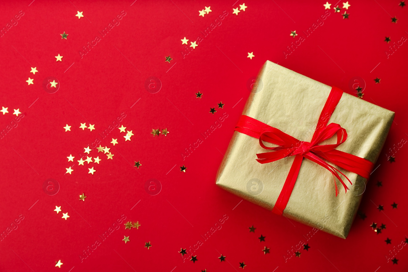 Photo of Golden gift box and shiny confetti on red background, top view. Space for text