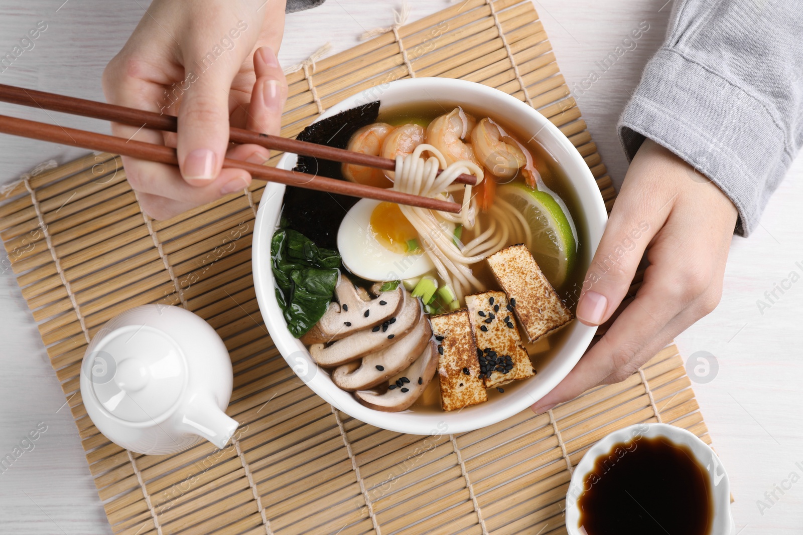 Photo of Woman eating delicious ramen with chopsticks at white table, top view. Noodle soup