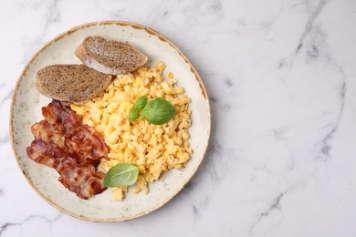 Delicious scrambled eggs with bacon and basil in plate on white marble table, top view. Space for text