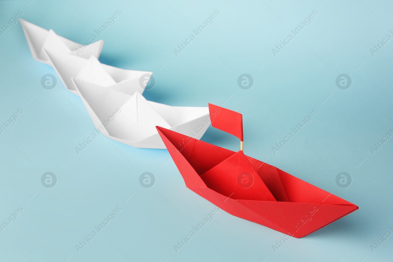 Photo of Group of paper boats following red one on light blue background. Leadership concept