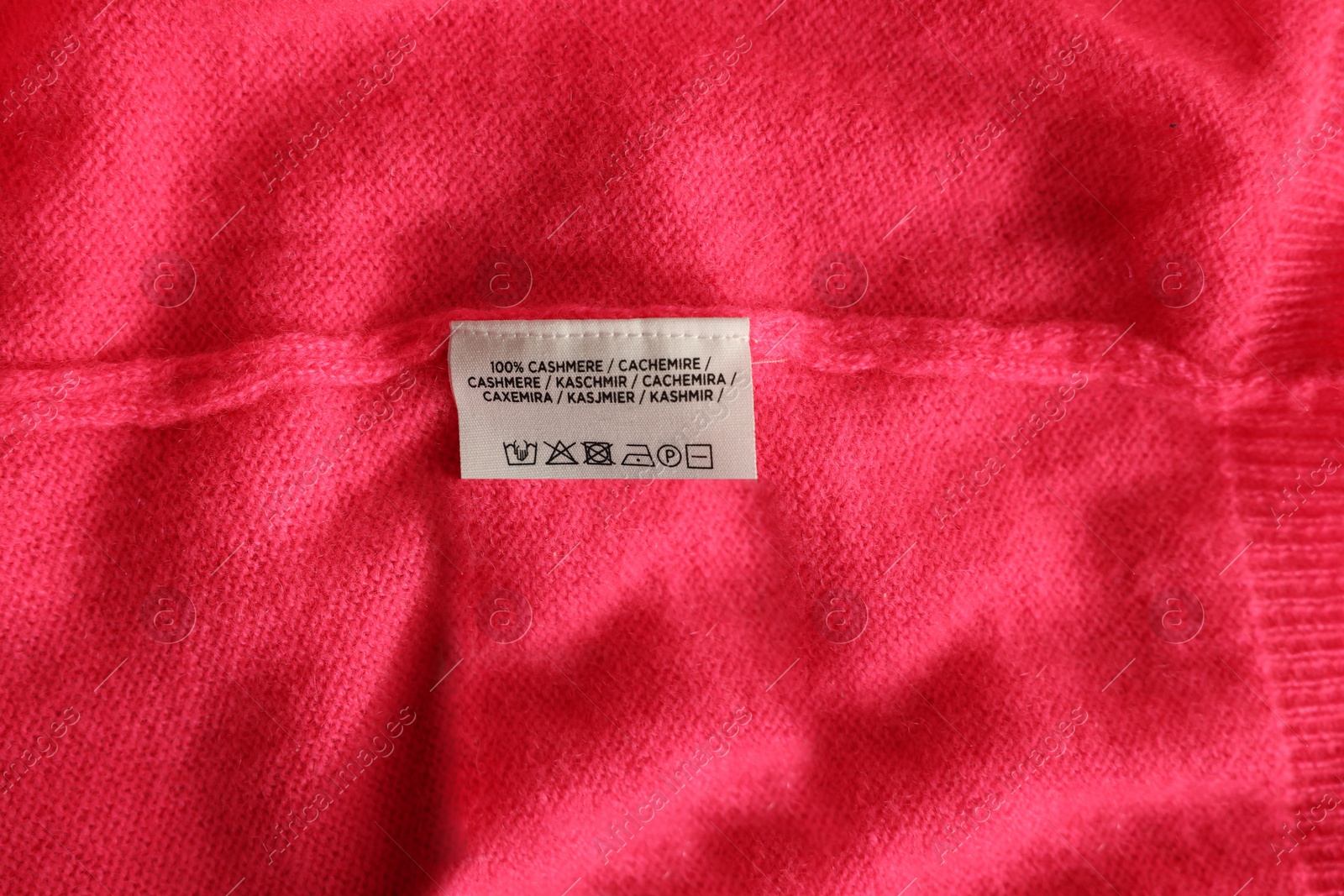 Photo of Clothing label in different languages on pink garment, top view