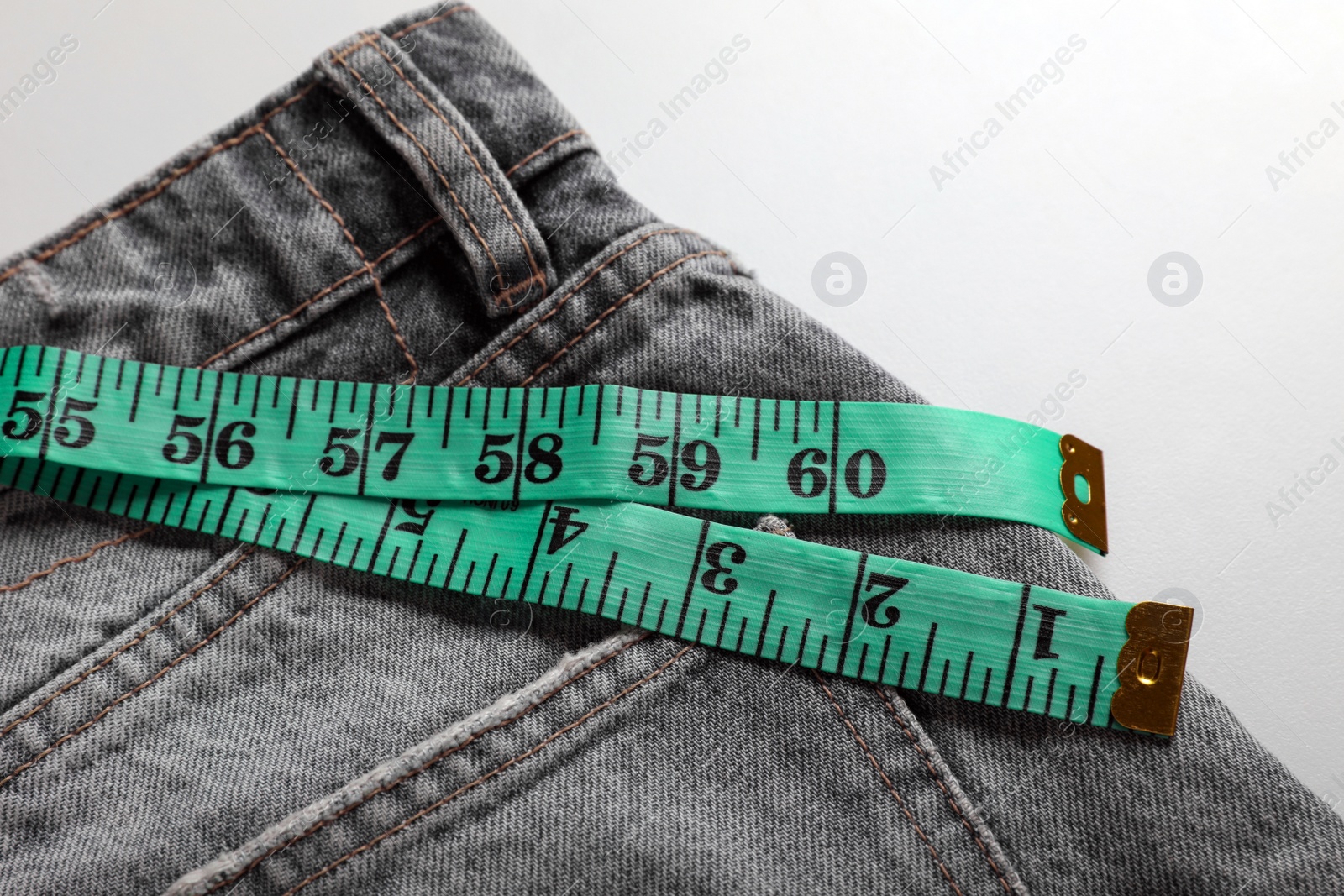 Photo of Jeans with measuring tape on light grey background, top view. Weight loss concept