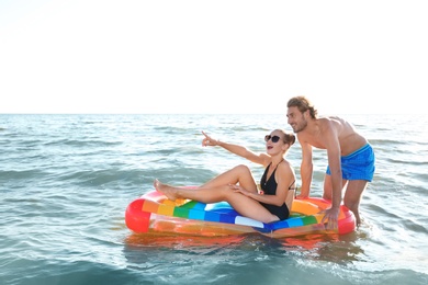 Photo of Happy young couple in beachwear swimming with inflatable mattress in sea
