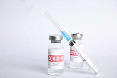 Photo of Vials with coronavirus vaccine and syringe on white background