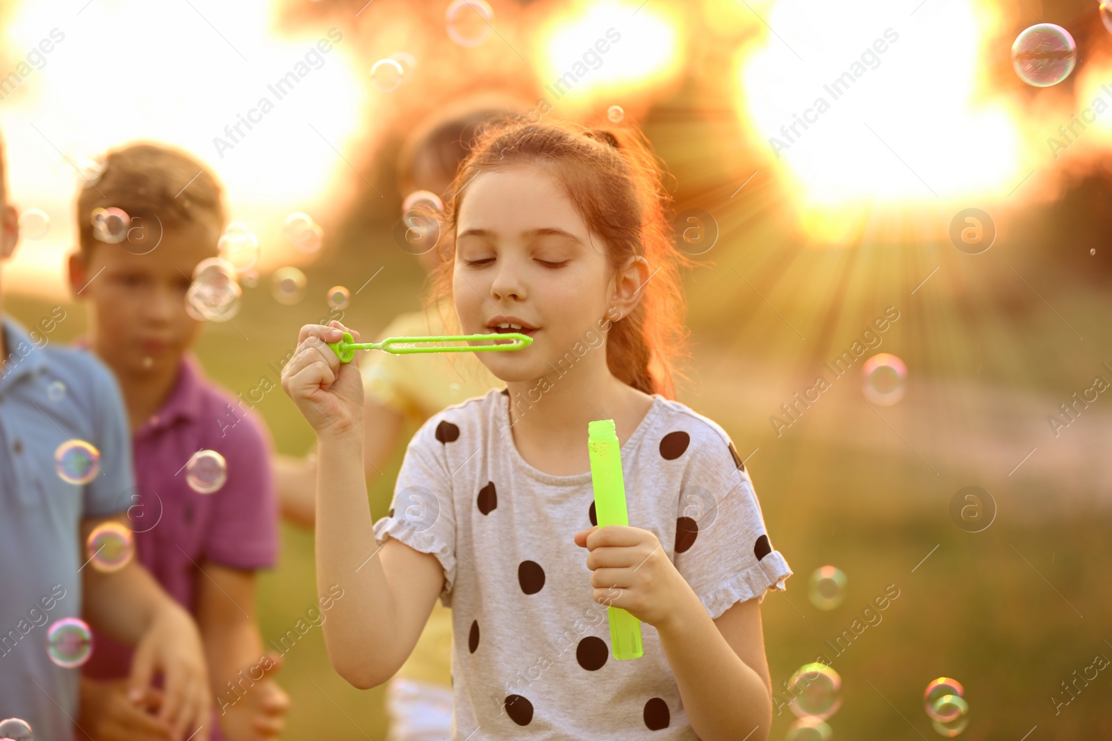 Image of Cute little girl blowing soap bubbles outdoors at sunset