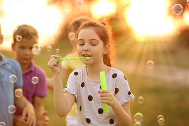 Cute little girl blowing soap bubbles outdoors at sunset