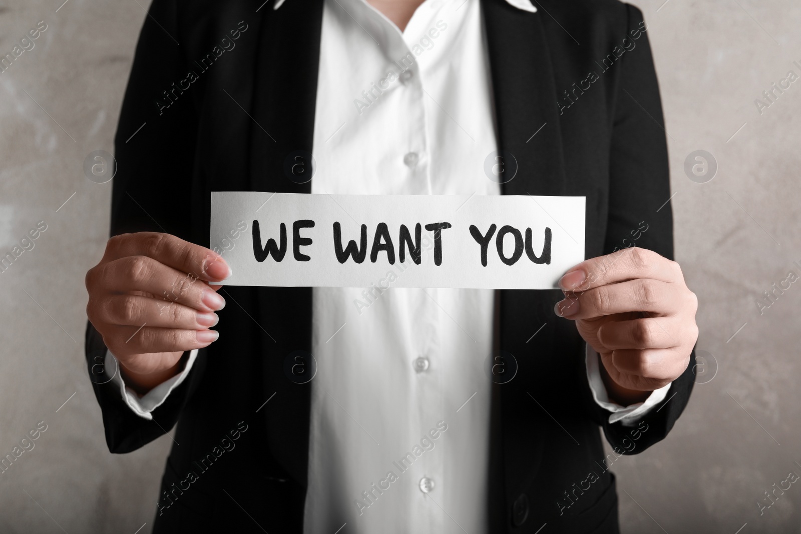 Photo of Woman holding sheet of paper with words WE WANT YOU on beige background, closeup. Career concept