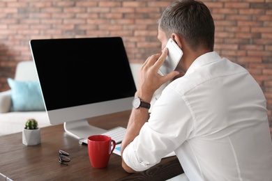 Photo of Young man talking on phone in home office. Time to work