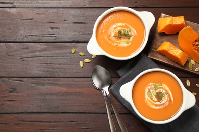 Photo of Tasty creamy pumpkin soup with dill and seeds in bowls on wooden table, flat lay. Space for text