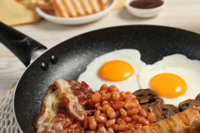 Frying pan with cooked traditional English breakfast on white table, closeup
