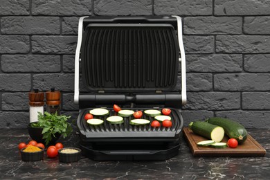 Photo of Electric grill with vegetables and spices on black marble table