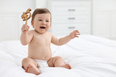 Photo of Cute baby boy with wooden rattle on bed at home. Space for text