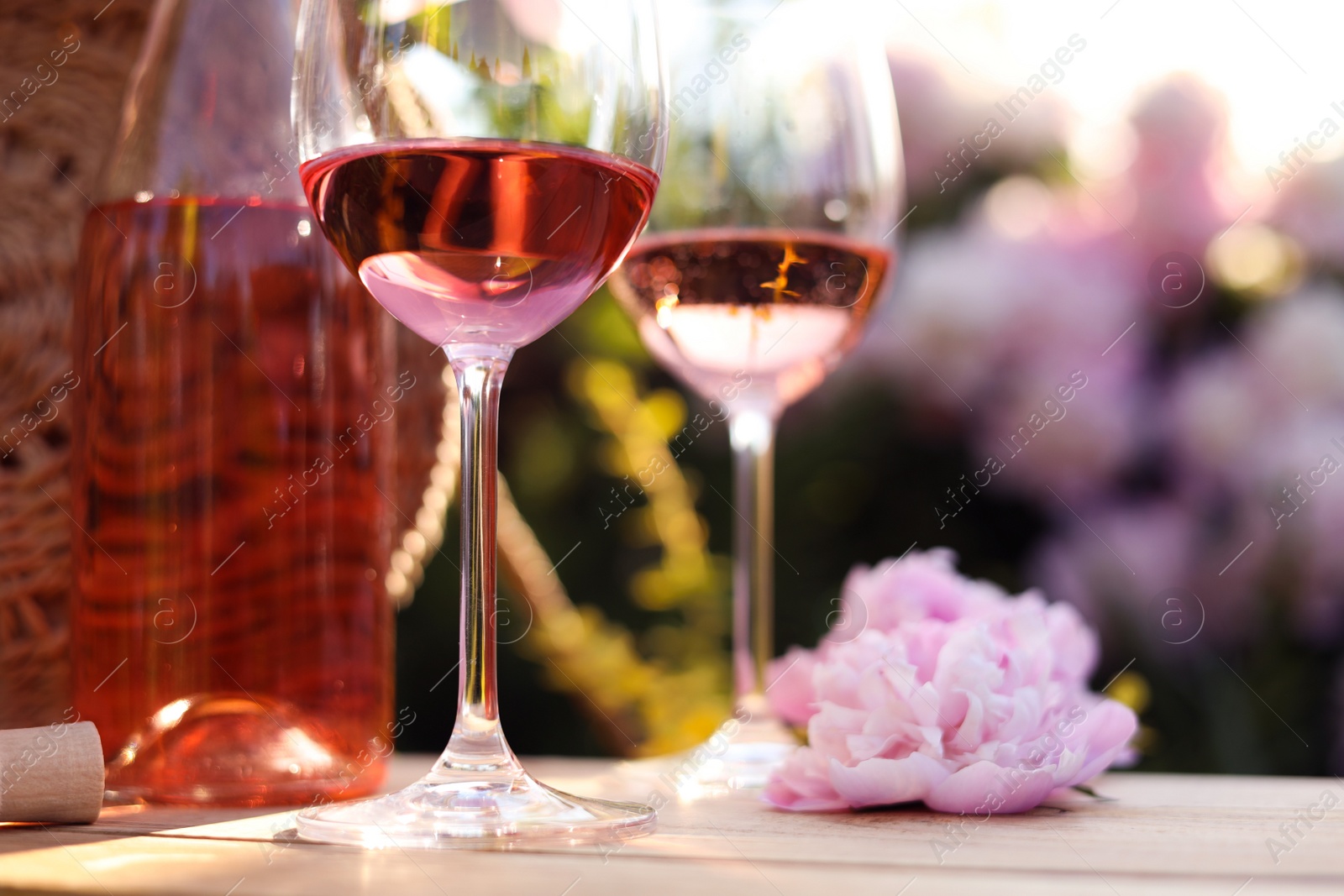 Photo of Bottle and glasses of rose wine near beautiful peony flower on wooden table in garden, closeup