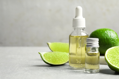 Photo of Lime essential oil and cut citrus fruits on light table. Space for text