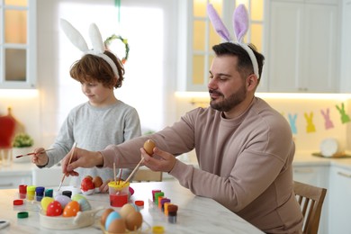 Easter celebration. Father with his little son painting eggs at white marble table in kitchen