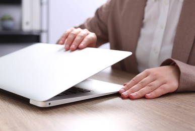 Woman opening laptop at wooden table in office, closeup