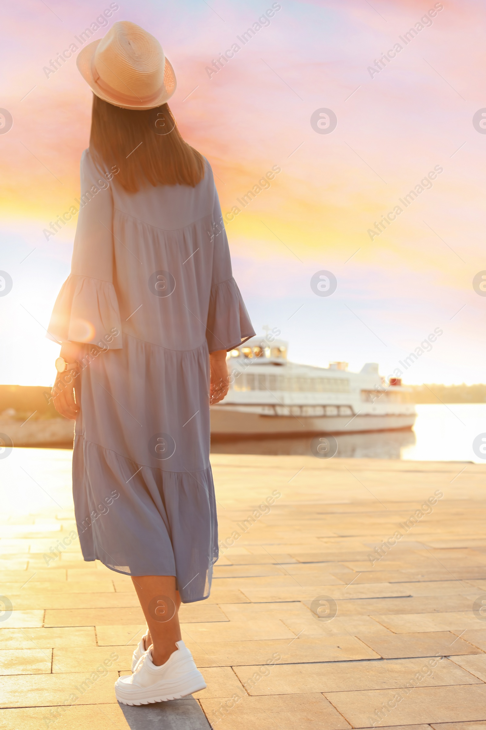 Photo of Young woman walking on pier at sunset light