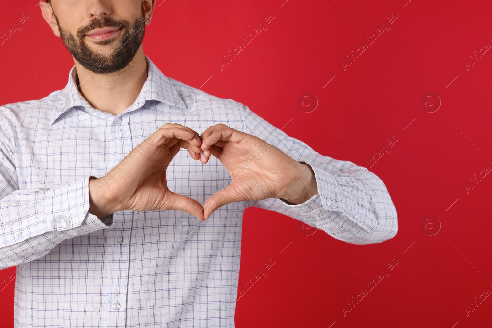 Photo of Man making heart with hands on red background, closeup