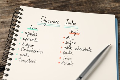Photo of List with products of low and high glycemic index in notebook and pen on wooden table, closeup