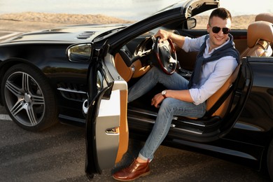 Photo of Handsome young man in luxury convertible car outdoors