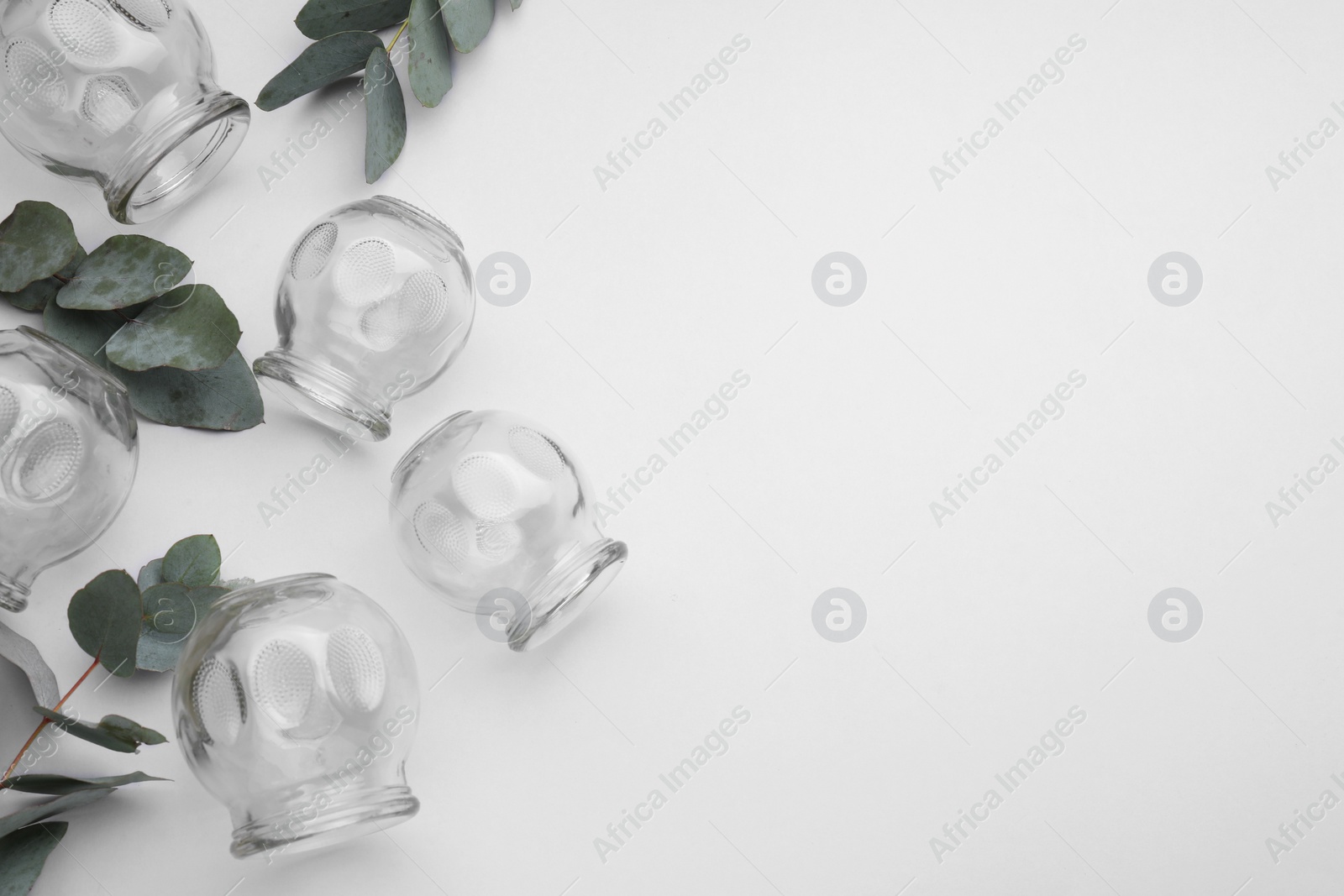 Photo of Glass cups and leaves on light grey background, flat lay with space for text. Cupping therapy