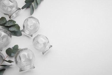 Glass cups and leaves on light grey background, flat lay with space for text. Cupping therapy