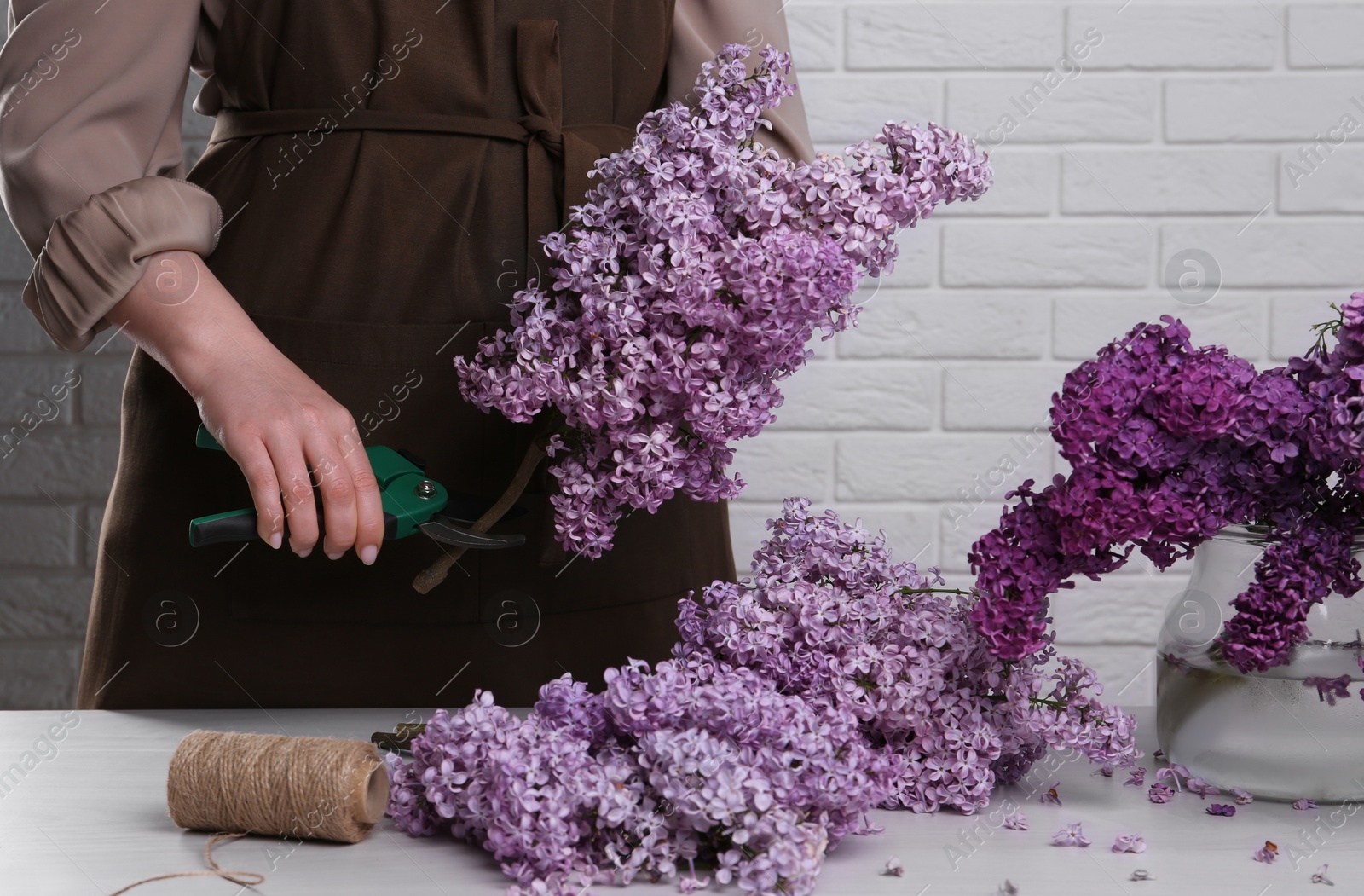 Photo of Woman trimming lilac branches with secateurs at white wooden table, closeup