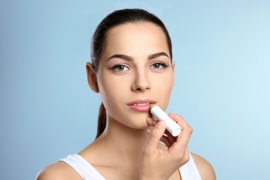 Young woman applying balm on her lips against color background