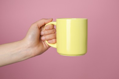 Photo of Woman holding yellow mug on pink background, closeup