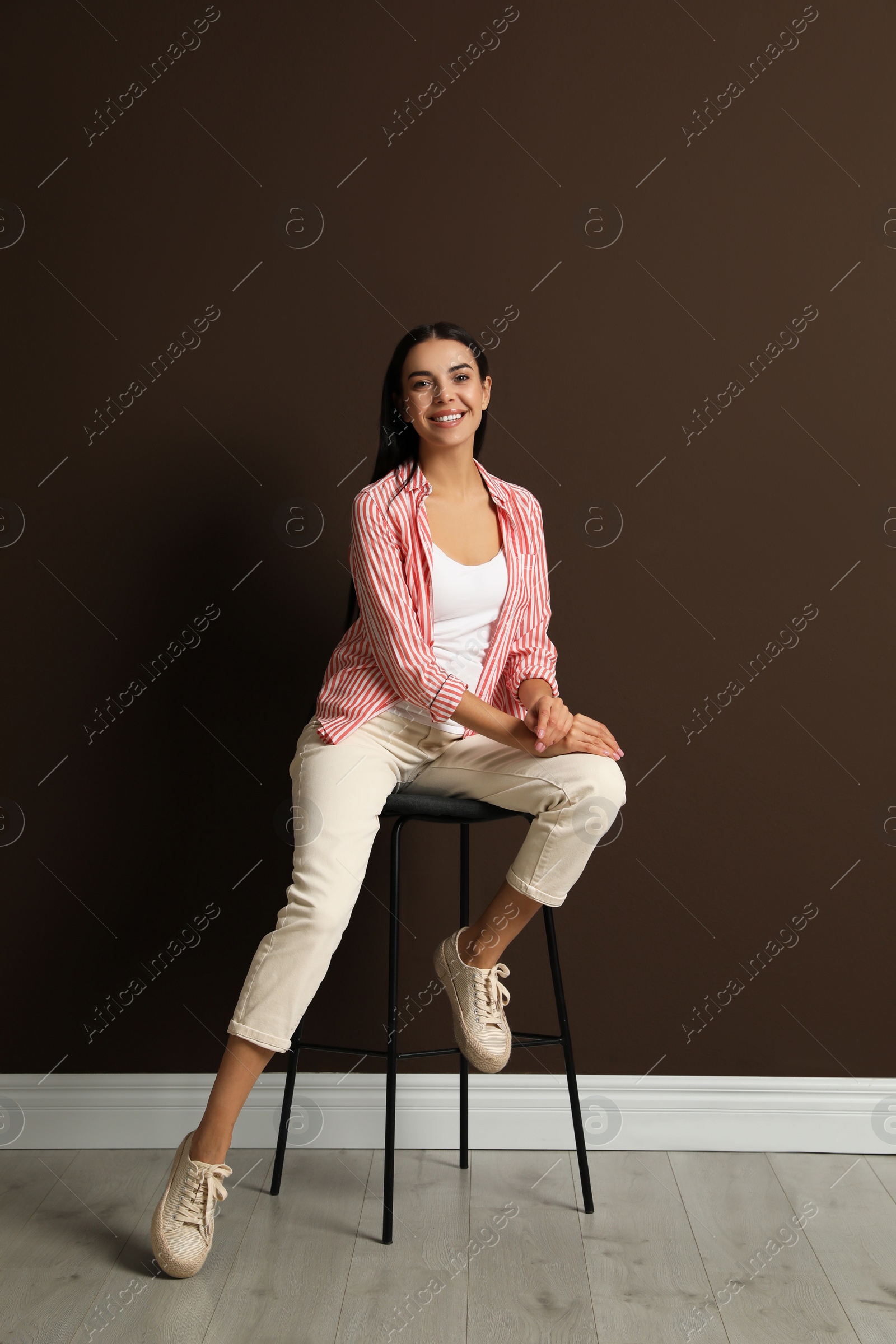 Photo of Beautiful young woman sitting on stool near brown wall