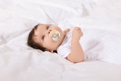 Photo of Cute little baby with pacifier lying on bed