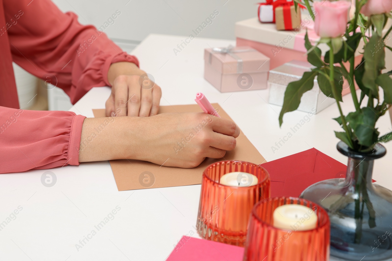 Photo of Young woman writing message in greeting card at white table, closeup