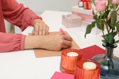 Young woman writing message in greeting card at white table, closeup