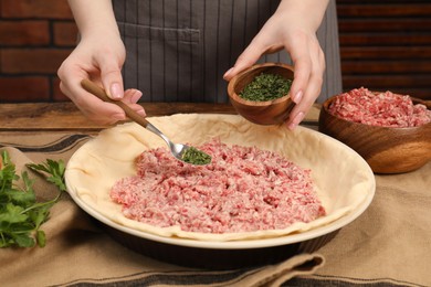 Photo of Woman putting greens into baking dish with dough to make meat pie at wooden table, closeup