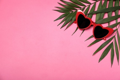 Photo of Stylish heart shaped glasses and tropical leaves on color background, flat lay. Space for text