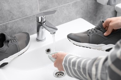 Photo of Woman washing stylish sneakers with brush in sink, closeup